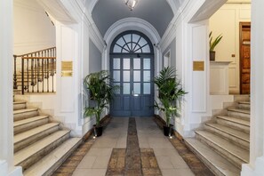 A grand hallway with a blue door, potted plants, and a staircase on either side.