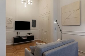 A living room with a flat-screen TV, a black entertainment unit, a grey sofa, a floor lamp, and a door.
