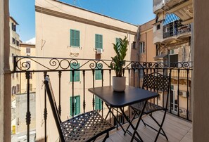 Ein Balkon mit Tisch und Stühlen, einem Topfpflanzen und Blick auf benachbarte Gebäude.