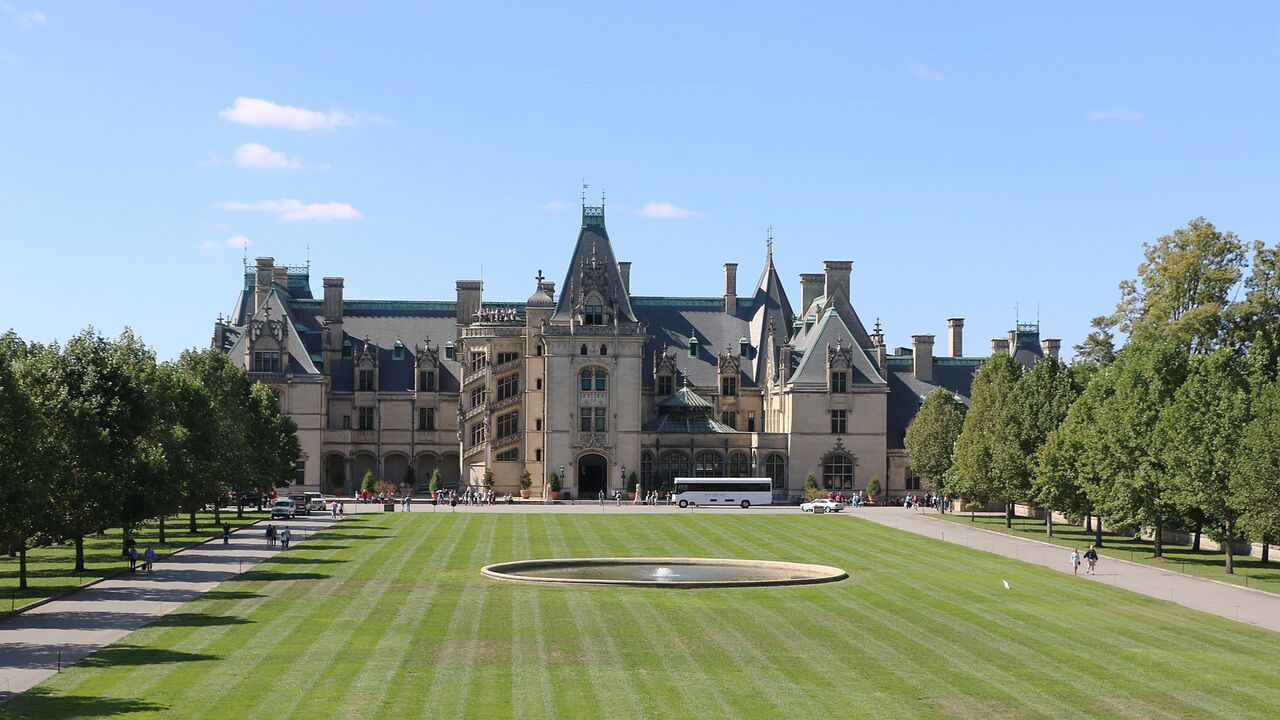 A large, historic building with a central courtyard, surrounded by trees and a well-maintained lawn.
