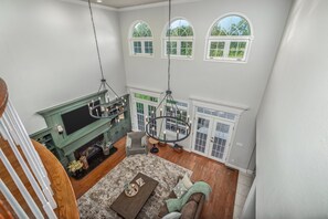 A spacious living room with a fireplace, a chandelier, and a view of the outdoors through arched windows.