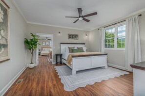 A bedroom with a bed, a ceiling fan, a window with curtains, and a potted plant.