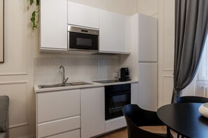 A modern kitchen with white cabinets, a built-in oven, a sink, and a coffee maker. There is a dining table with chairs and a plant on the wall. - Castro Pretorio 9 - FromHometoRome (Roma)