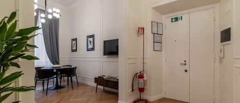 Habitación de hotel con comedor, televisión, extintor y puerta con letrero de salida de emergencia.