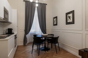 Een praktische keuken met een eethoek, met een ronde tafel met stoelen, een koffieapparaat en een radiator.