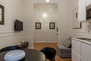 A modern living room with a dining table, black chairs, a grey sofa, a small kitchen area, and a chandelier. - Castro Pretorio 9 - FromHometoRome (Roma)
