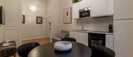 A modern kitchen with white cabinetry, a black dining table with a bowl centerpiece, and a chandelier.