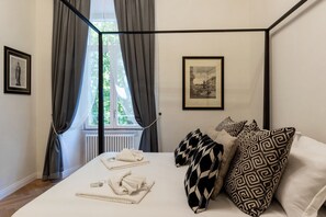 A neatly made bed with towels and a black and white patterned pillow, a framed picture on the wall, and a window with curtains. - Castro Pretorio 9 - FromHometoRome (Roma)