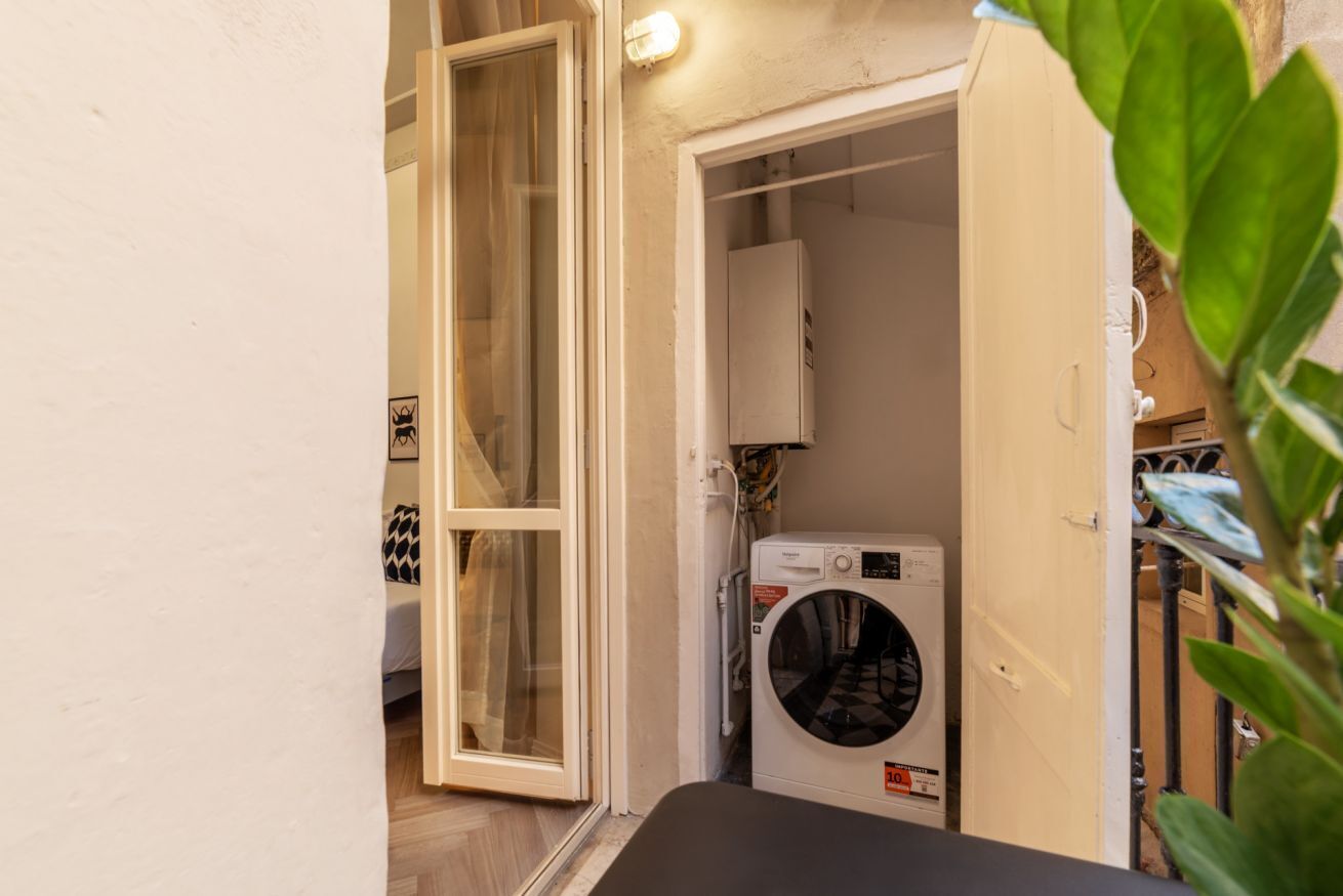 Un área de lavandería con lavadora y secadora, una puerta que da a otra habitación, y una planta al frente.
