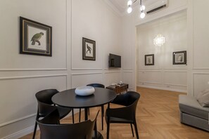A dining area with a round table and chairs, framed artwork on the walls, a chandelier, and a television. - Castro Pretorio 9 - FromHometoRome (Roma)