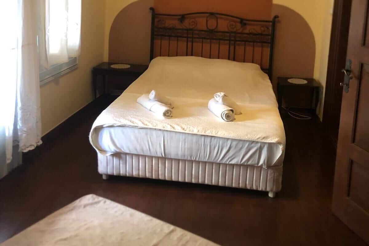 A neatly made bed with two rolled towels, a wooden headboard, and a small bedside table with a lamp.