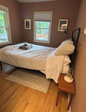 A bedroom with a bed, a nightstand, a lamp, and two windows. - The Beau at Belle-eau-Claire beach (Tiny)