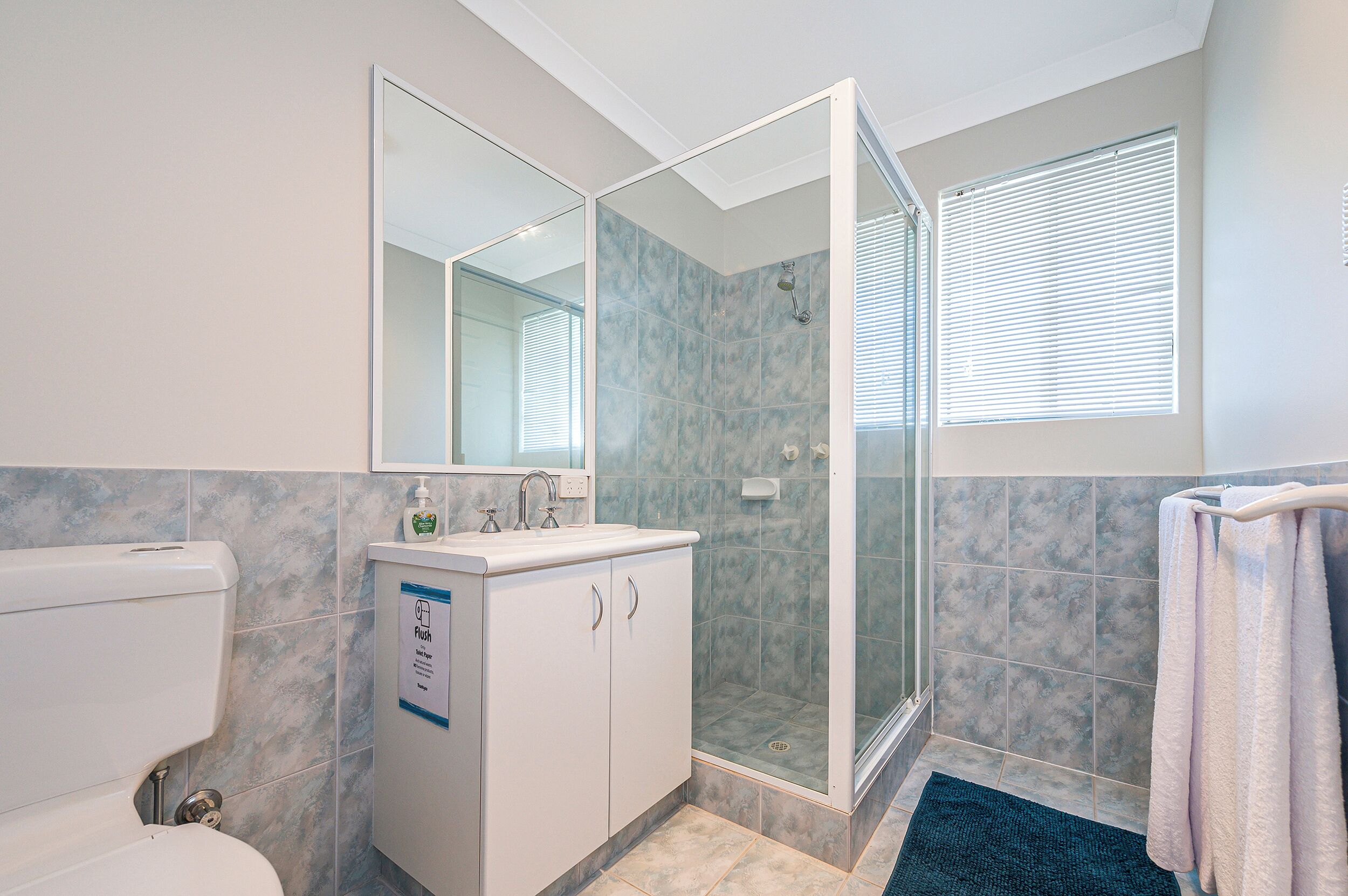 A bathroom with a toilet, sink, mirror, shower, and towel rack.