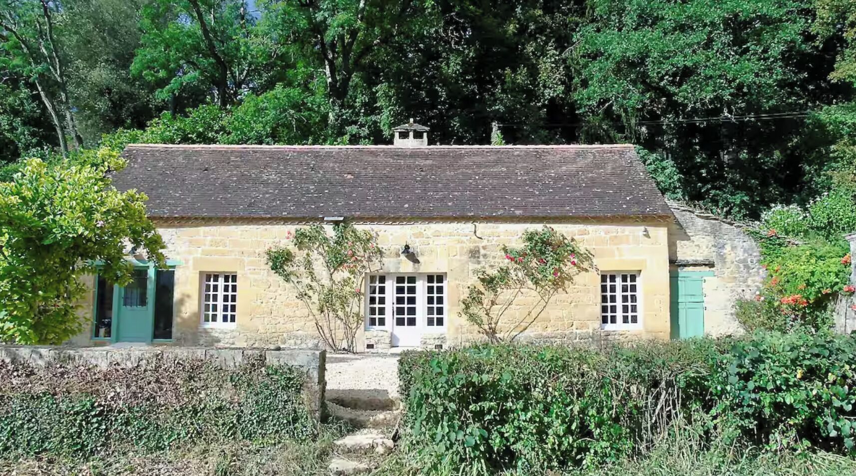 A stone house with a sloped roof, a small staircase leading to the entrance, and a garden in front.