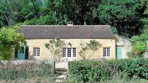Uma casa de pedra com telhado inclinado, uma pequena escadaria que leva à entrada e um jardim na frente.