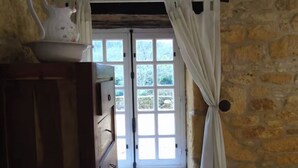 Quarto com parede de pedra, um armário de madeira, janela com cortinas e porta que dá para o exterior.