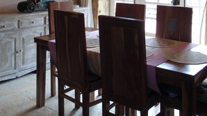 Uma sala de jantar com mesa, cadeiras, lustre, parede de pedra e janela com cortinas.