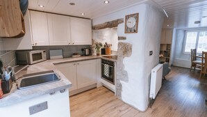 A kitchen with white cabinets, a microwave, a sink, a stove, and a clock on the wall. - Tamarisk Cottage (St. Agnes)