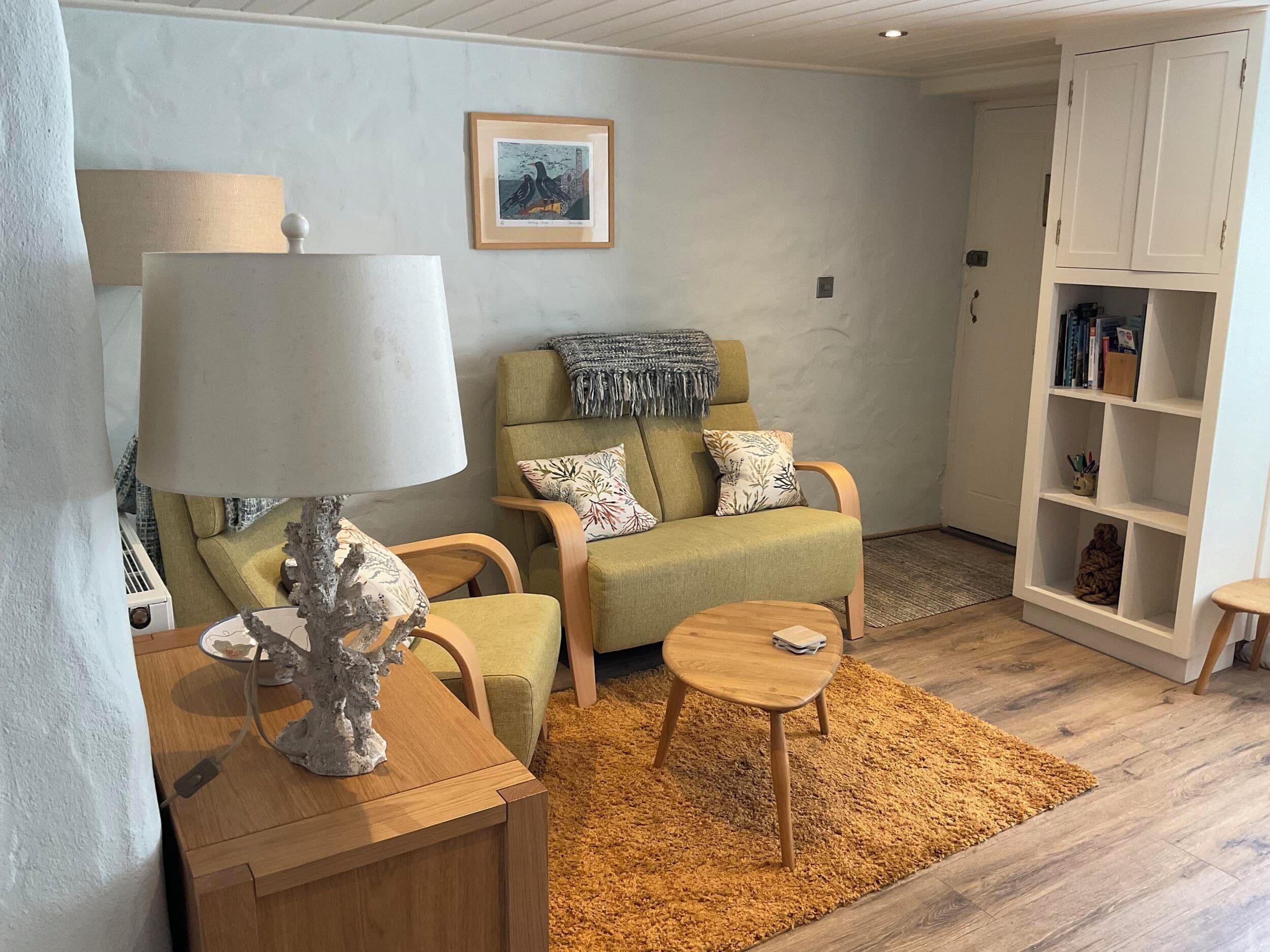 A living room with a sofa, armchairs, a coffee table, a lamp, a bookshelf, and a framed picture on the wall.