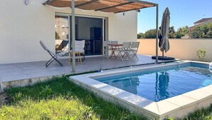 A modern house with a swimming pool, a covered patio with chairs and a table, and a door leading to an interior space. - New villa with private pool in the heart of the village - sleeps 4 (Suze-la-Rousse)