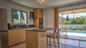 A modern kitchen with wooden cabinets, a central island, and a dining area with bar stools. - New villa with private pool in the heart of the village - sleeps 4 (Suze-la-Rousse)