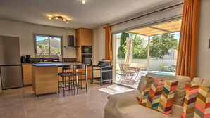 A modern kitchen with a dining area, a sofa with patterned cushions, and a sliding glass door to a balcony. - New villa with private pool in the heart of the village - sleeps 4 (Suze-la-Rousse)