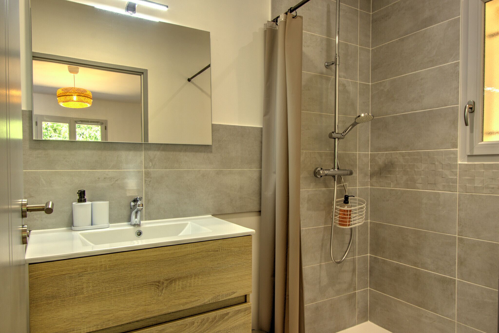A bathroom with a sink, mirror, shower, and wooden vanity.