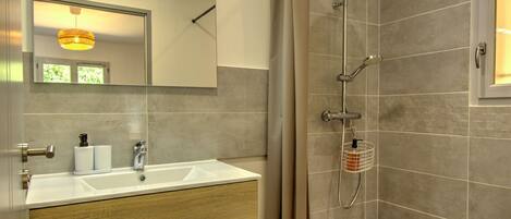 A bathroom with a sink, mirror, shower, and wooden vanity.