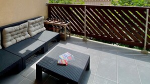 A covered outdoor seating area with a sofa and a coffee table, a wooden fence, and a view of buildings and trees. - Carcans - 3 bedrooms near ocean + Parking (Carcans)