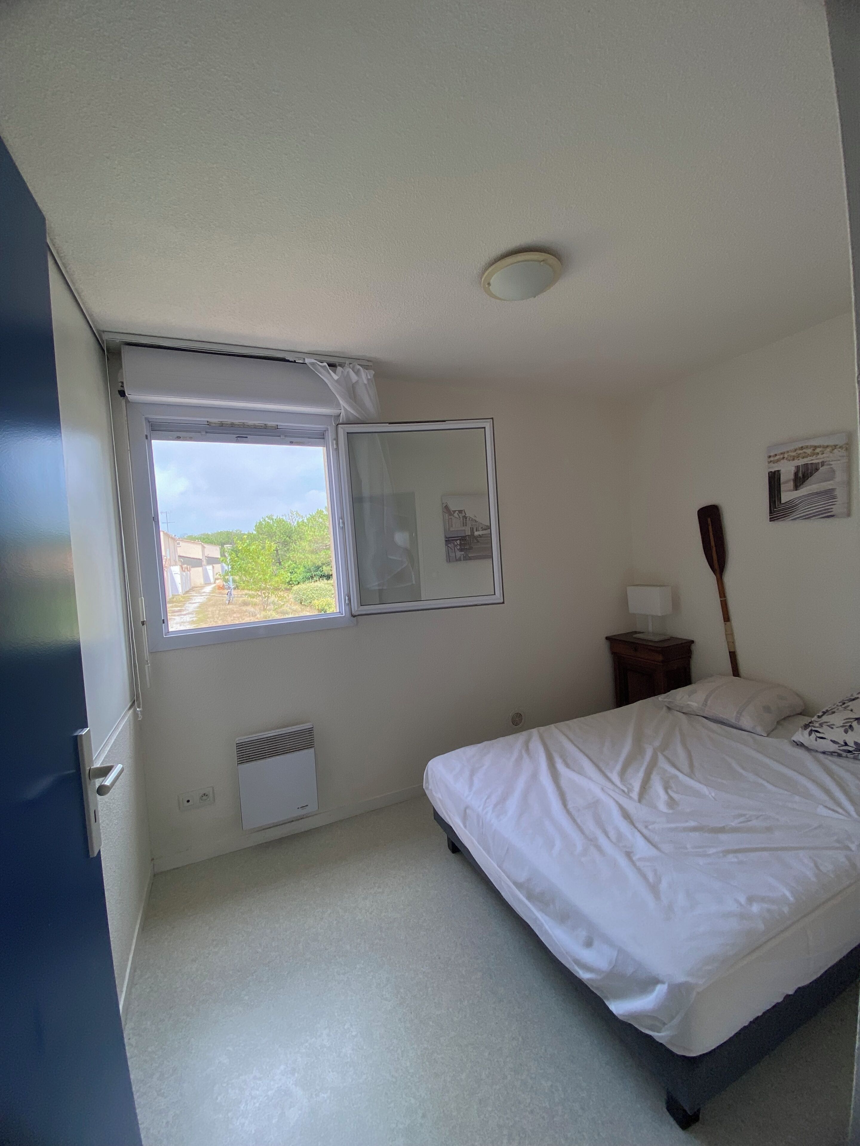 Un dormitorio con una cama individual, una ventana, una mesita de noche con lámpara y un cuadro colgado en la pared.