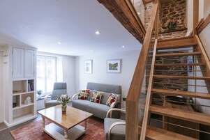 Una sala de estar moderna con un sofá gris, una mesa de centro de madera y una escalera con paredes de piedra.