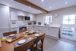 Una cocina moderna con armarios blancos, una mesa de comedor de madera preparada para el desayuno y un reloj en la pared.