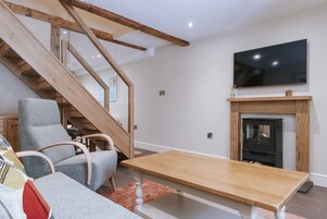 Una sala de estar con una escalera, un televisor de pantalla plana, una chimenea y una mesa de madera.