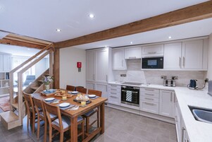 A modern kitchen with white cabinets, a wooden dining table, and a built-in oven.