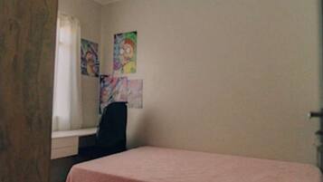 A room with a bed, a desk, and a chair. There are two colorful paintings on the wall.
