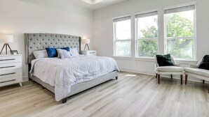 Ein modernes Schlafzimmer mit einem großen Bett, zwei Nachttischen, einem Sessel und großen Fenstern.