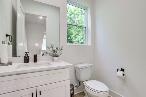 A bathroom with a white toilet, a sink with a mirror, and a window with a view of trees.