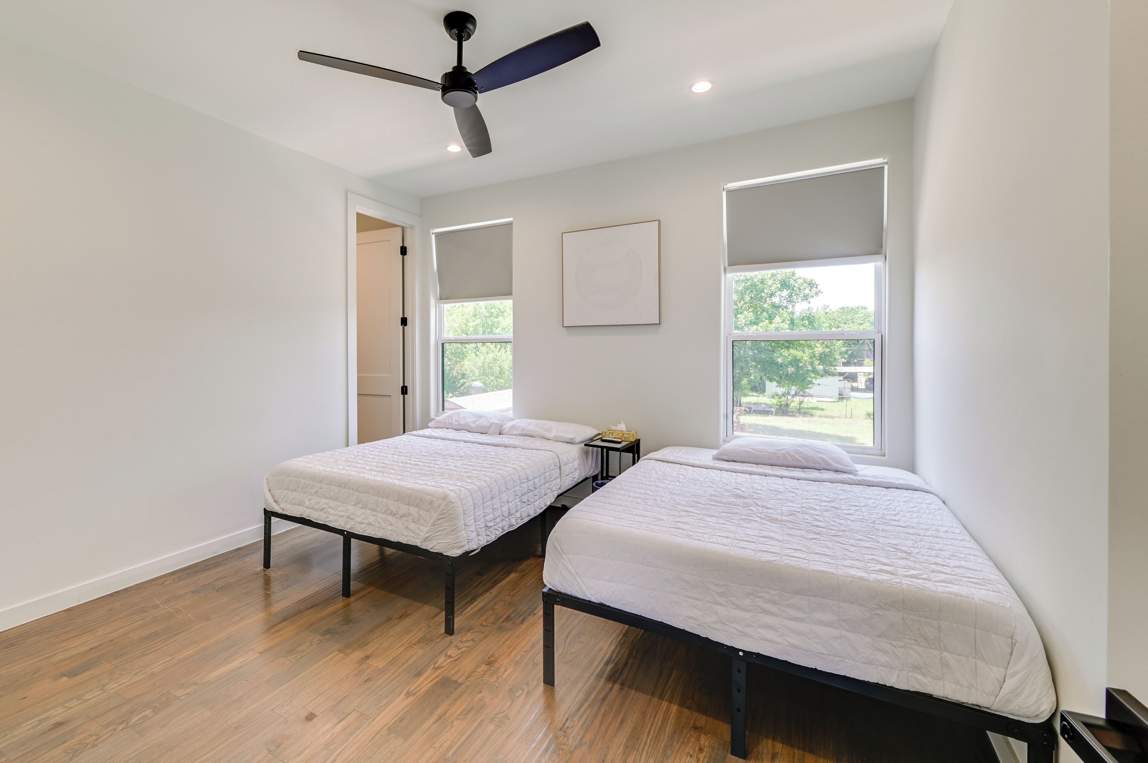 Habitación con dos camas individuales, ventilador de techo y ventanas amplias con vistas a la vegetación.
