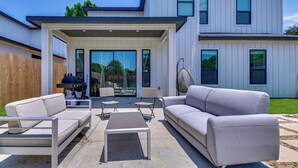 A modern two-story house with a covered patio area featuring outdoor furniture, including a sofa, chairs, and a table. - Modern & Spacious Home 3 Mi to Downtown Dallas! (Dallas)
