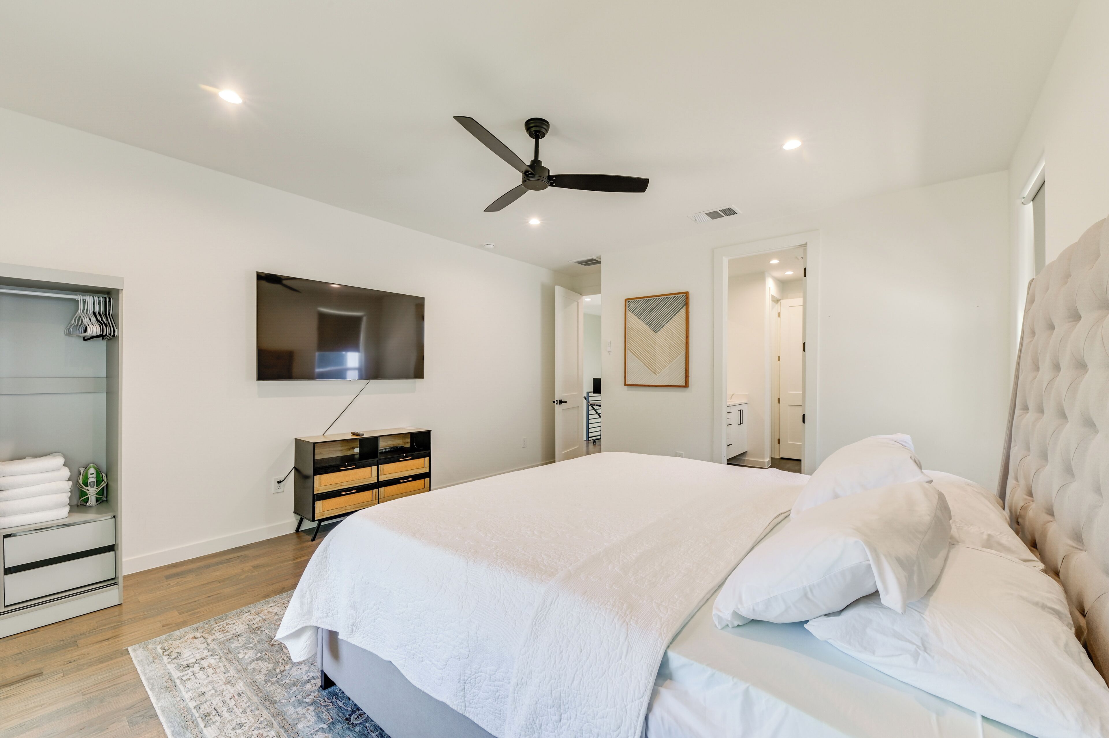 A modern bedroom with a large bed, a ceiling fan, a TV mounted on the wall, and a walk-in closet.