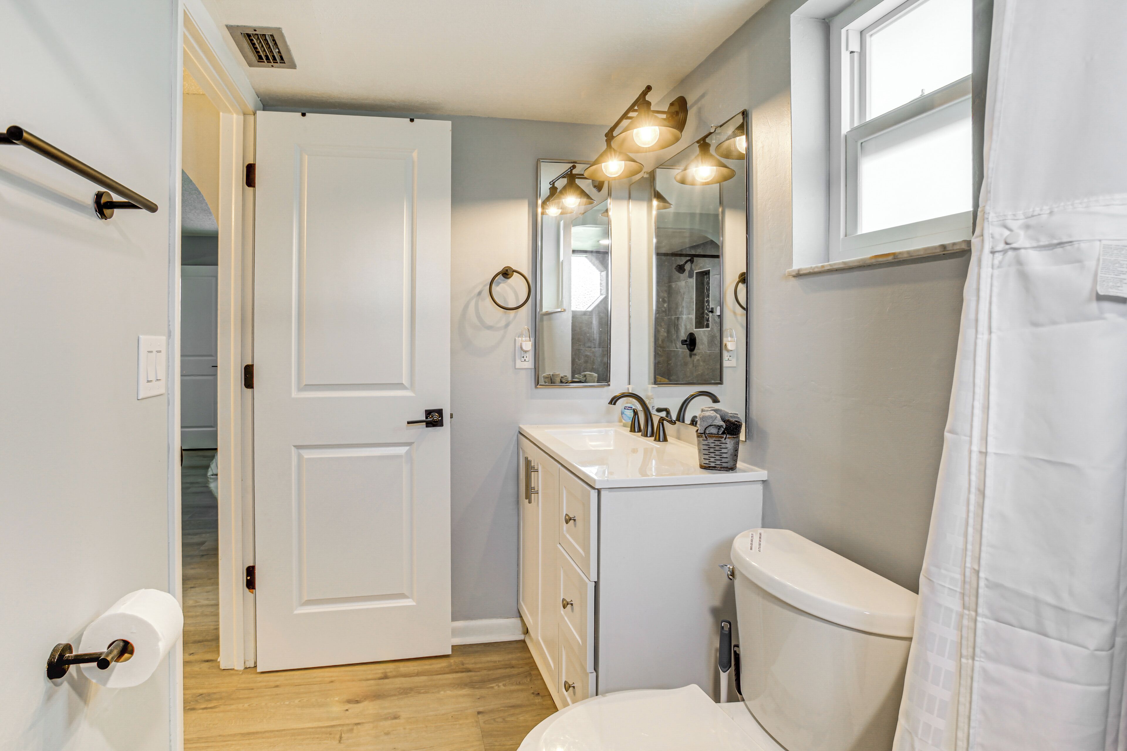 A bathroom with a toilet, sink, and mirror, featuring a shower curtain and a door leading to another room.
