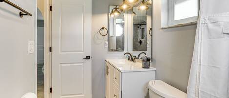 A bathroom with a toilet, sink, and mirror, featuring a shower curtain and a door leading to another room.