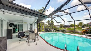 A covered outdoor swimming pool area with a glass ceiling, seating, and a view of the surrounding landscape. - Swim, Hike & Golf: Family Gem in Cape Coral! (Cape Coral)