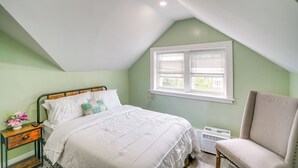 Un dormitorio con cama, mesita de noche, silla, ventana y radiador.