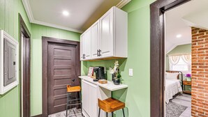 Una cocina compacta con armarios blancos, un taburete de madera y una cafetera.