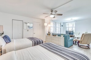 Een slaapkamer met twee bedden, een bureau, een stoel, een televisie en een plafondventilator.