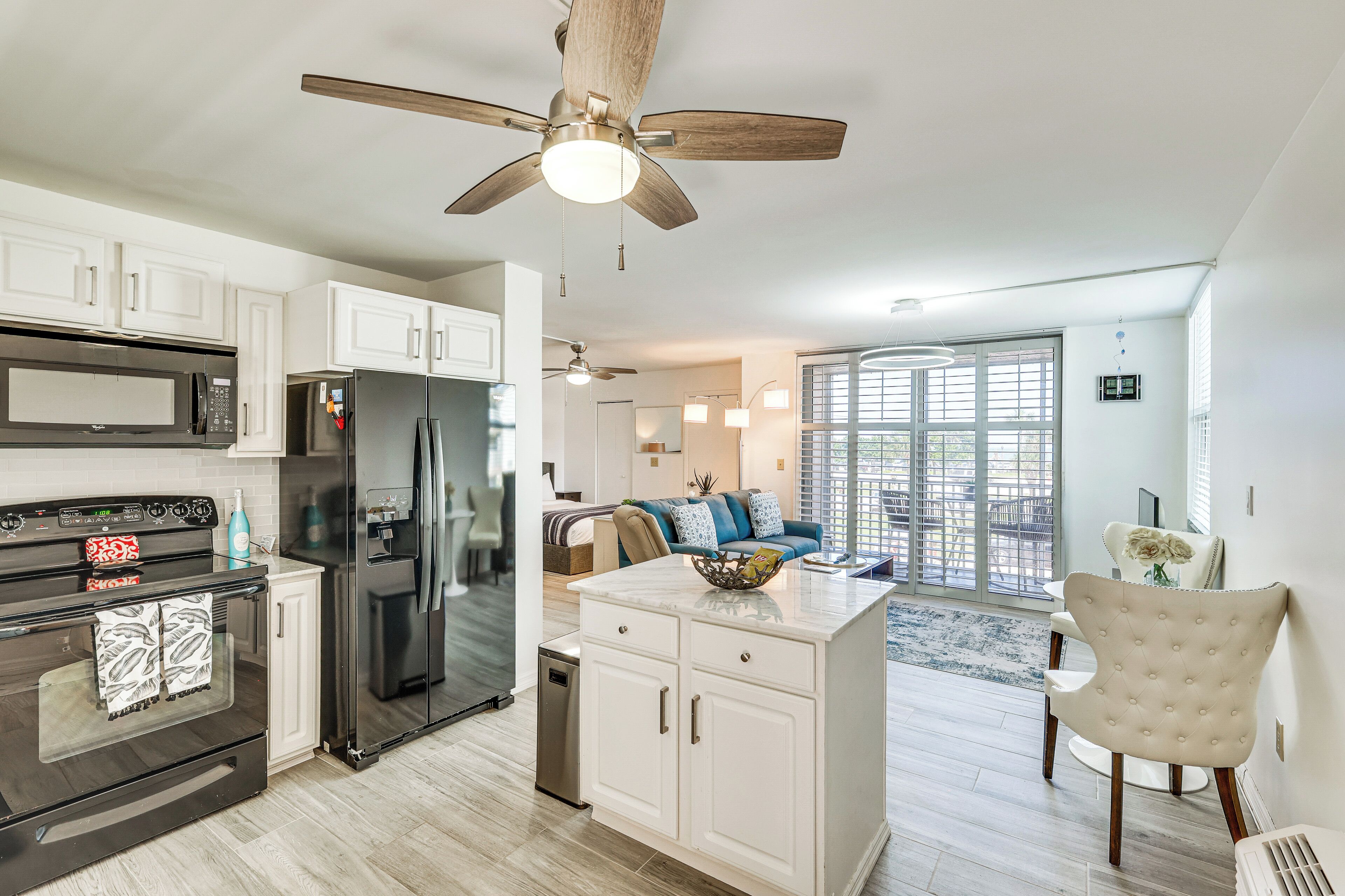 A modern kitchen with a built-in oven, microwave, and refrigerator, leading to a living area with a sofa and a dining table.