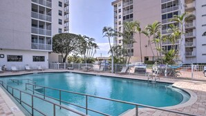 A swimming pool surrounded by a white fence, with palm trees and a multi-story building in the background. - Walk to Gulf: Bonita Springs Studio w/ Pool! (Bonita Springs)