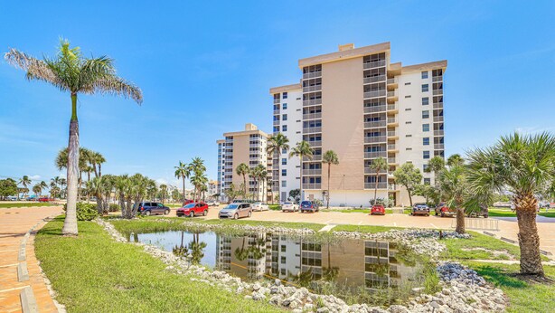 A high-rise hotel with multiple balconies, a landscaped garden with palm trees, and a small pond. - Walk to Gulf: Bonita Springs Studio w/ Pool! (Bonita Springs)