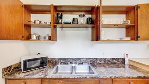 A kitchen with a double sink, a microwave, and wooden cabinets. - Walk to Food & Art: Condo in Historic Riverside (Jacksonville)